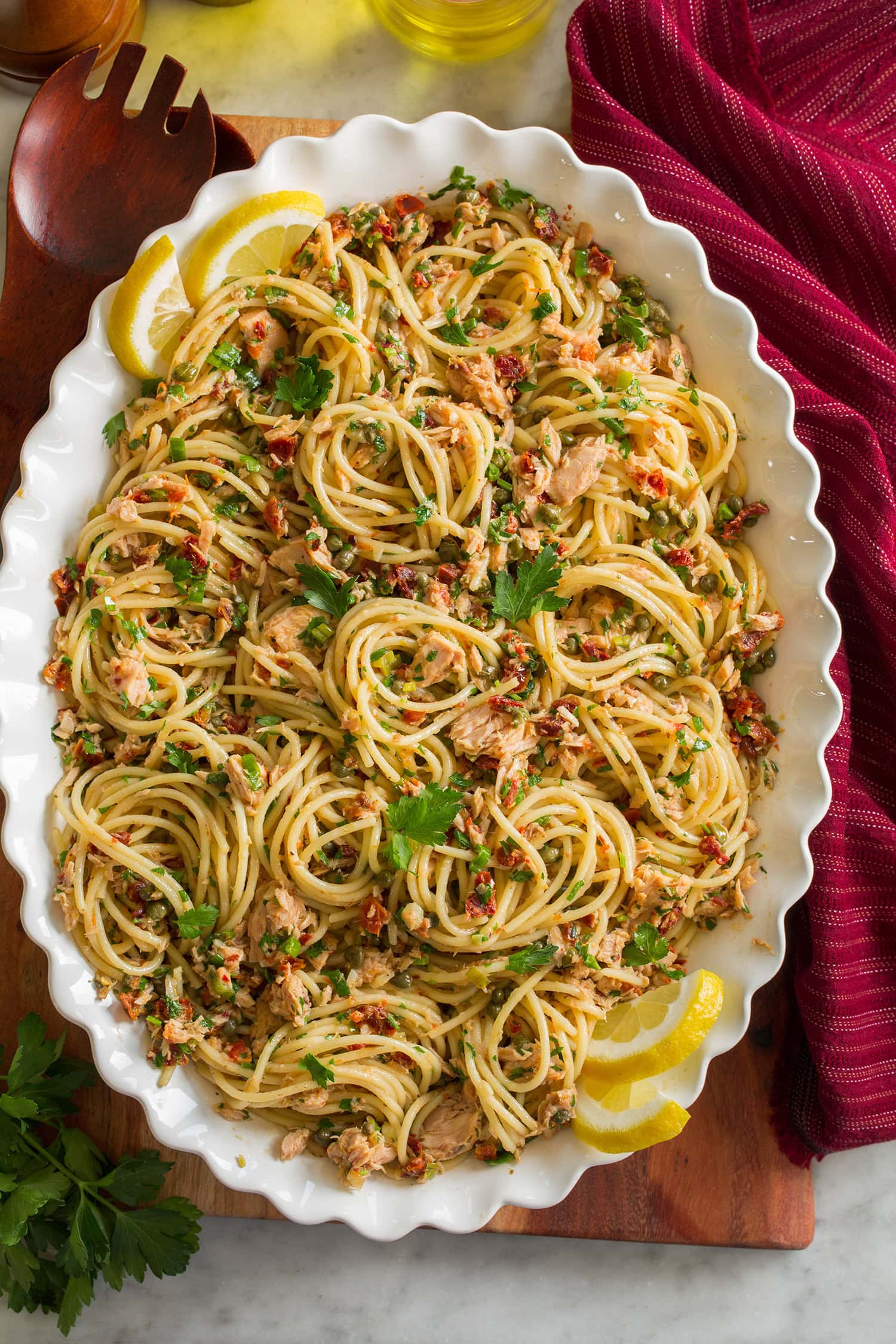Overhead photo of tuna pasta made with spaghetti noodles, canned tuna, capers, and sun dried tomatoes in a scalloped white bowl.