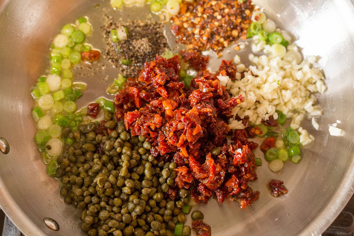 Sun dried tomatoes, capers, green onions, garlic, and red pepper flakes added to oil in saute pan.