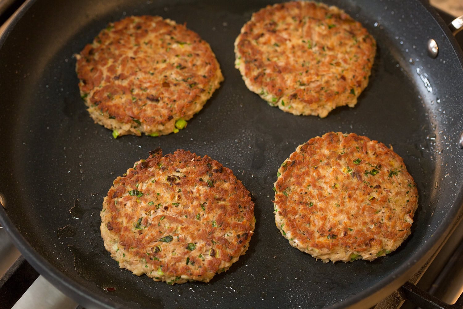 Tuna patties shown after cooked and golden brown in a dark non-stick skillet.