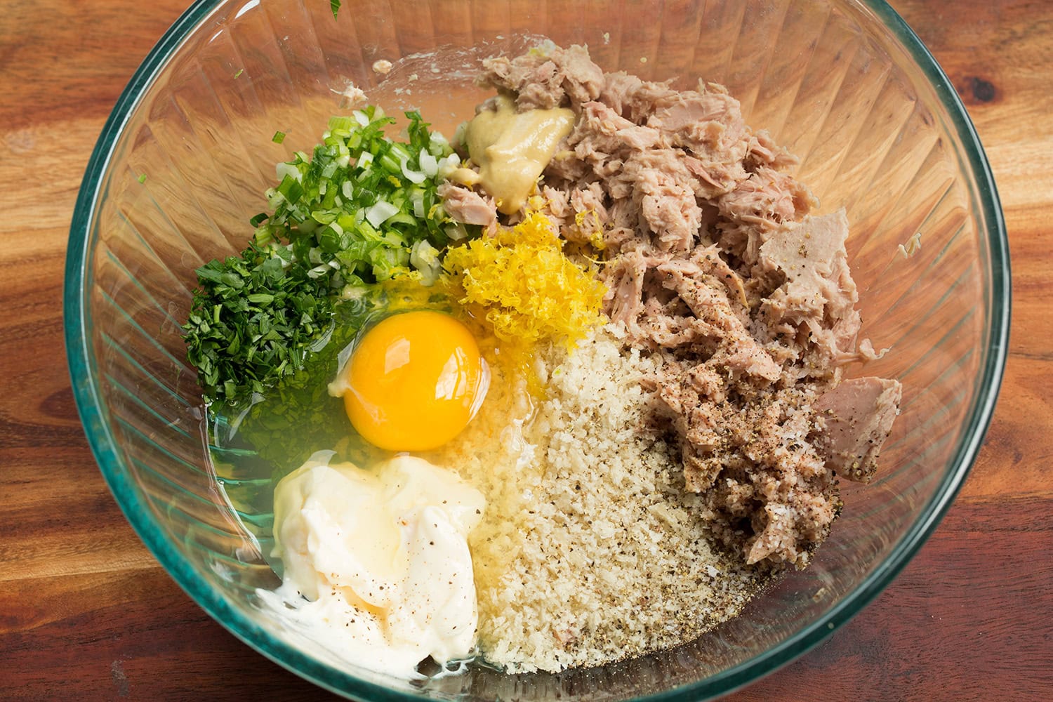 Tuna patty mixture of tuna, egg, panko bread crumbs, mayonnaise, parsley, green onions, lemon zest and juice shown in a mixing bowl before stirring.