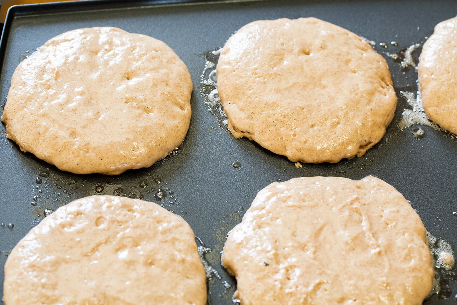 Cinnamon Roll Pancakes Pancakes shown poured onto griddle in circles, cooking on first side.