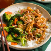 Slow cooker honey garlic chicken shown served over steamed white rice with broccoli and carrots to the side.