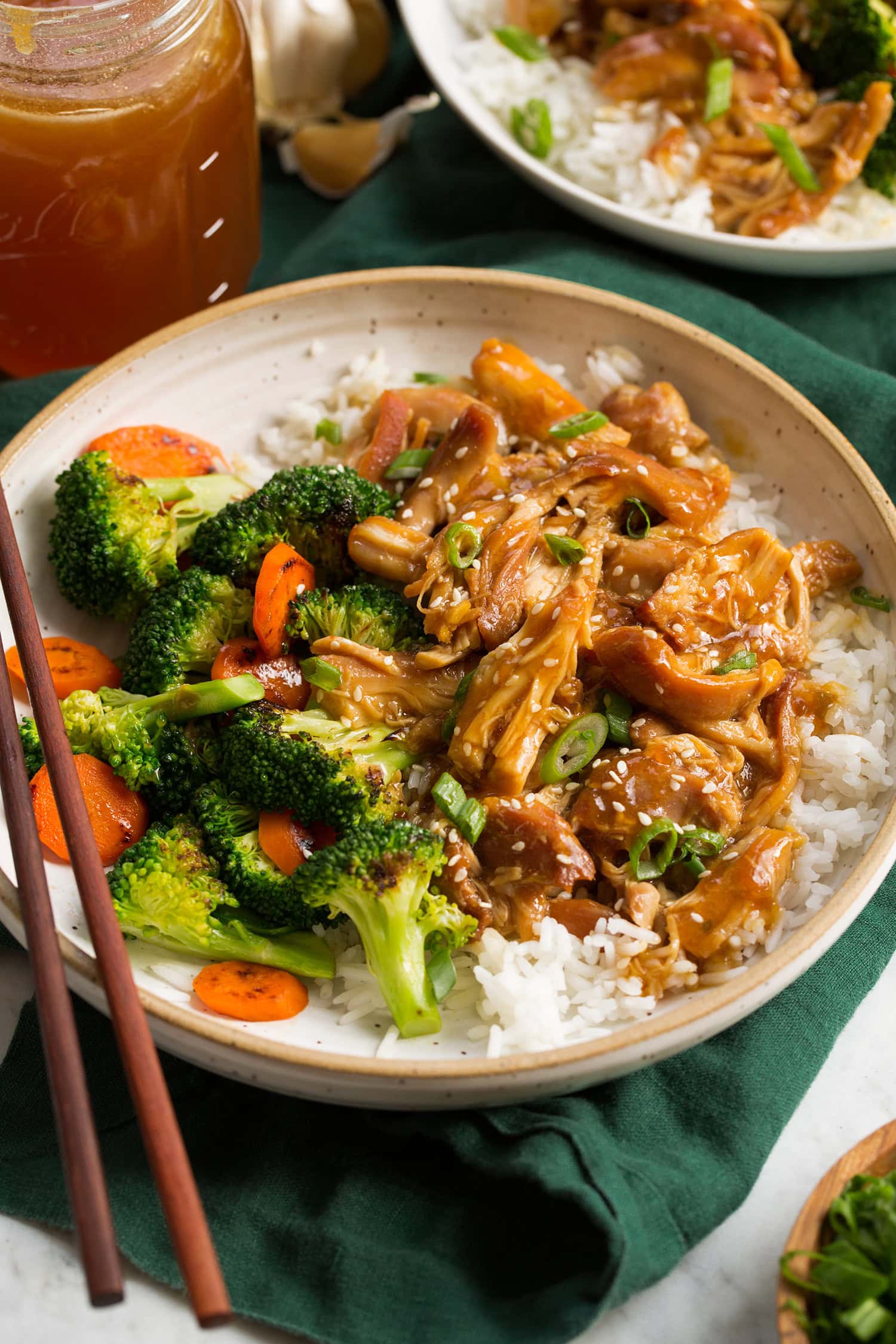 Slow cooker honey garlic chicken shown served over steamed white rice with broccoli and carrots to the side.