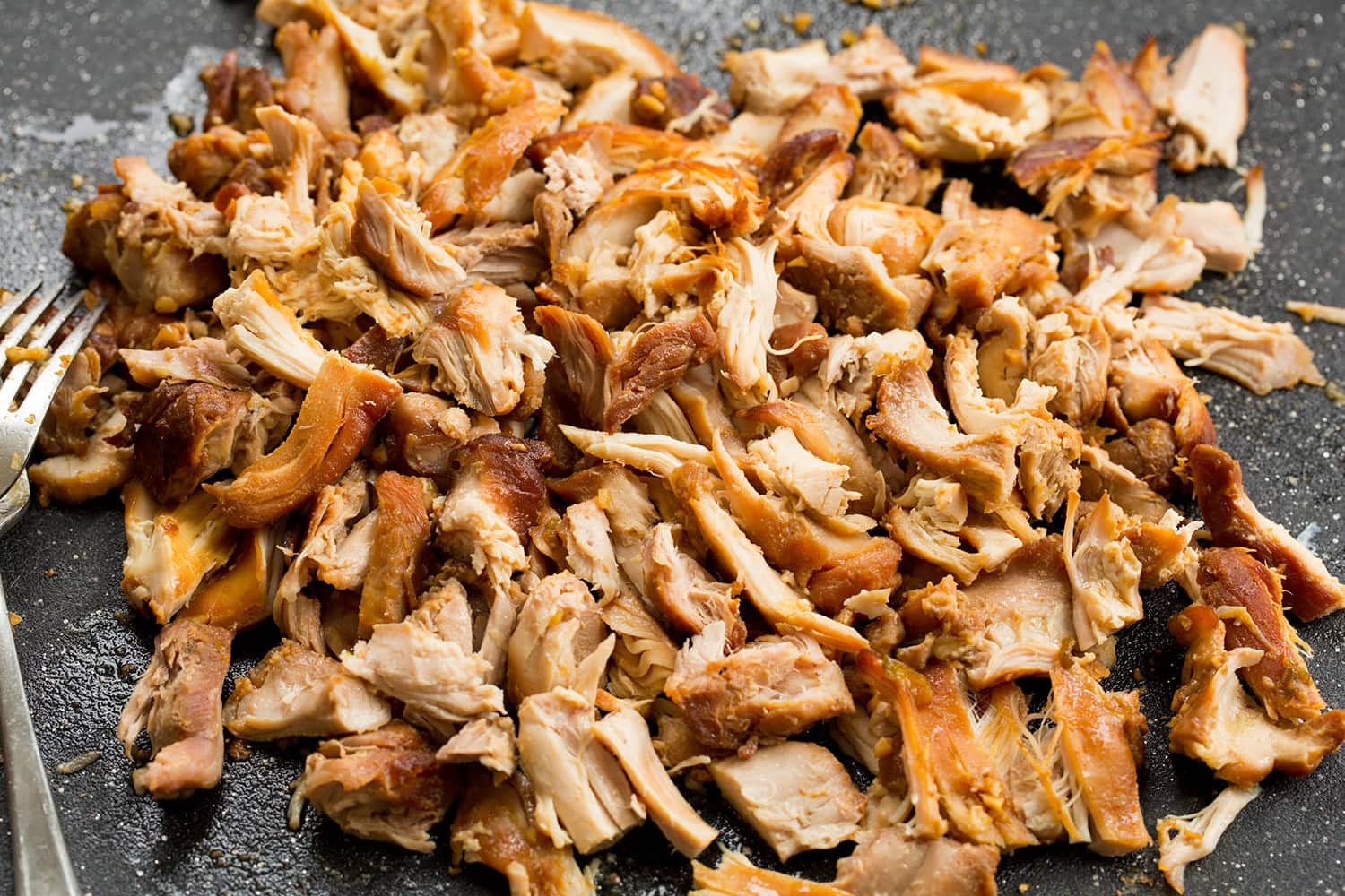 Shredded slow cooker chicken thighs shown on a cutting board.