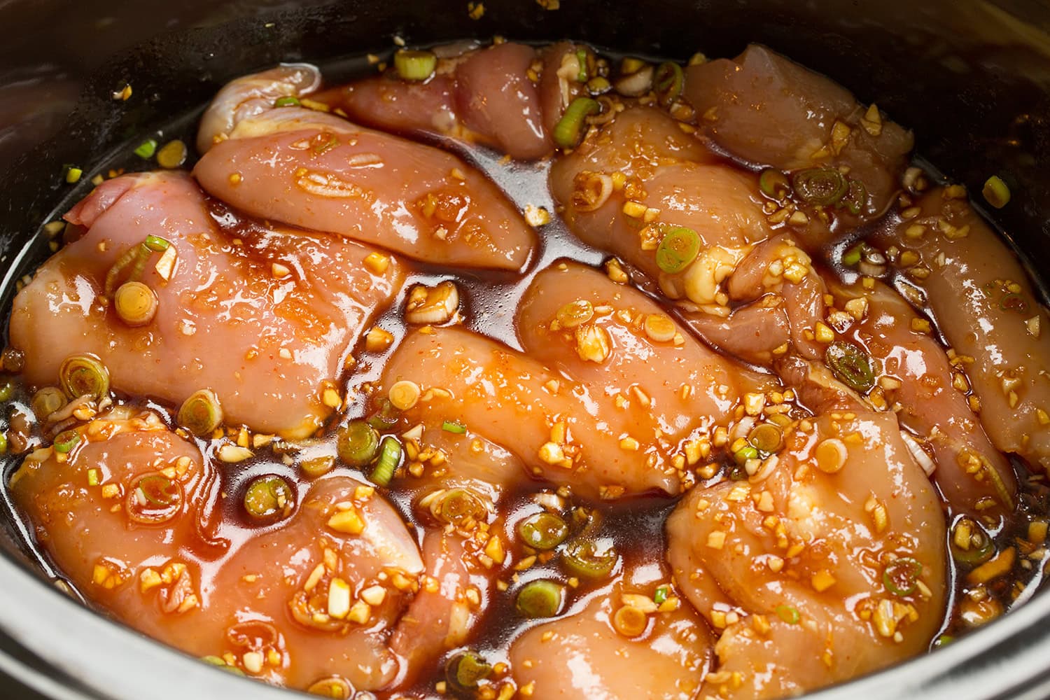 Raw chicken thighs shown with honey garlic sauce poured over in a slow cooker.