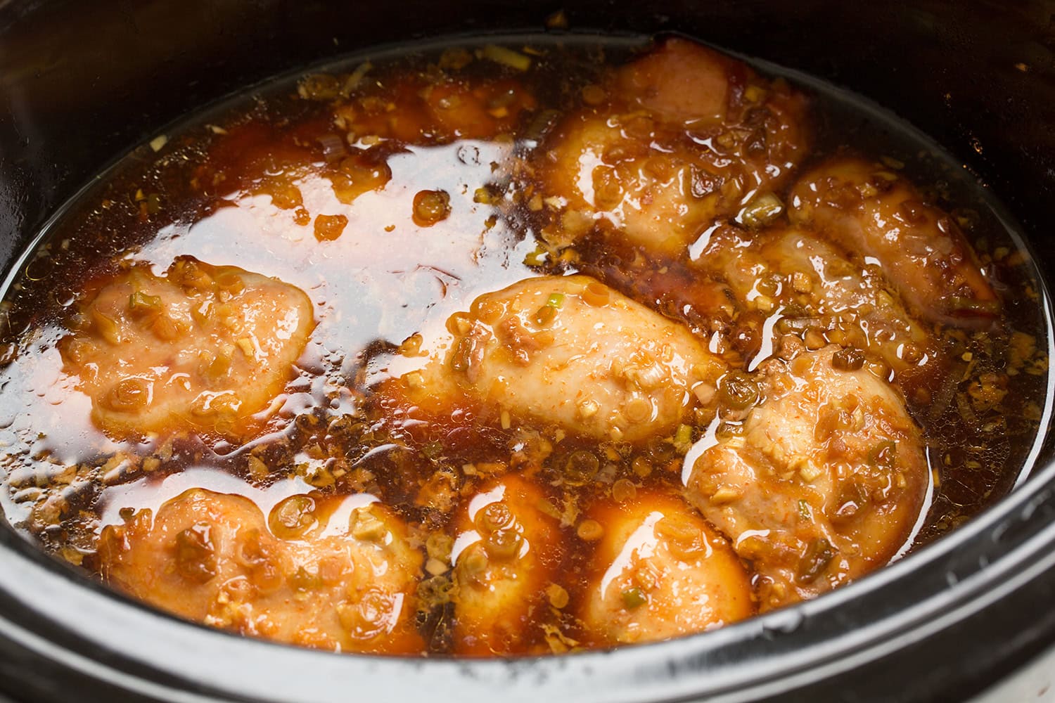 Chicken thighs with sauce shown cooked in the slow cooker before shredding and thickening the sauce.